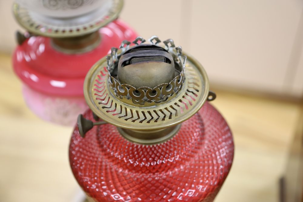 A brass column oil lamp with cranberry glass reservoir and frilled frosted and pink glass shade and a similar oil lamp